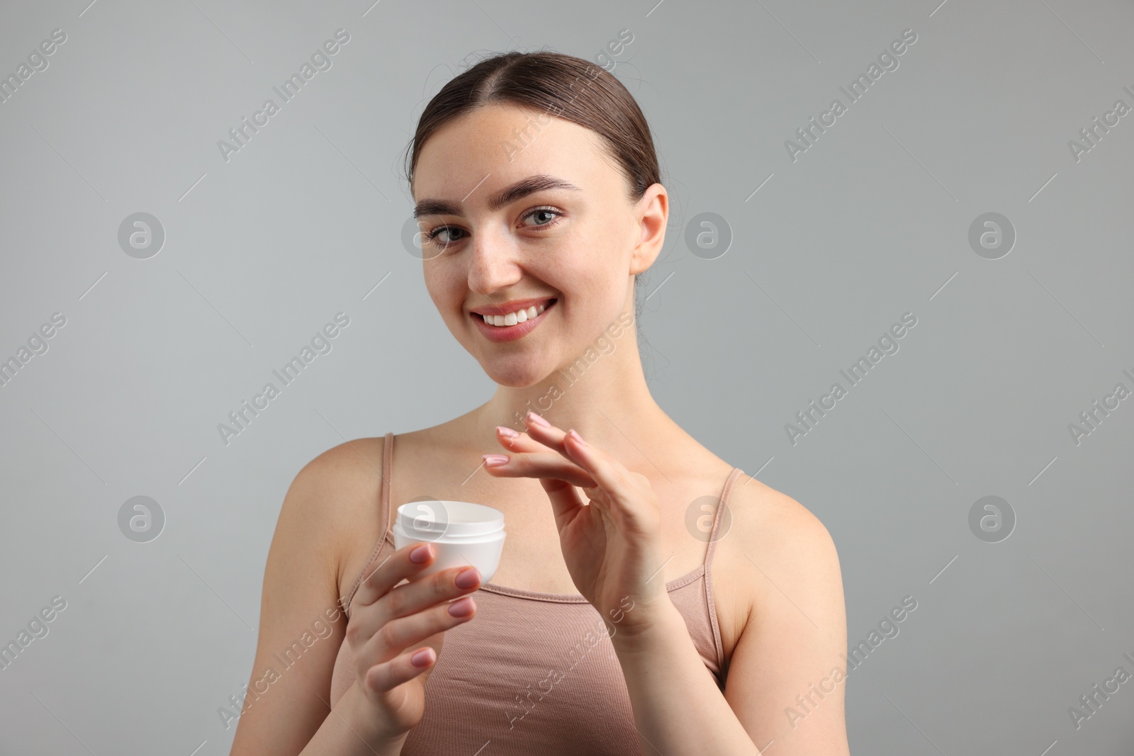 Photo of Beautiful woman with jar of face cream on gray background