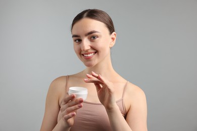 Photo of Beautiful woman with jar of face cream on gray background