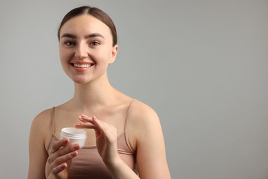 Photo of Beautiful woman with jar of face cream on gray background. Space for text
