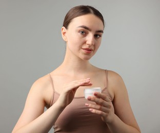 Photo of Beautiful woman with jar of face cream on gray background