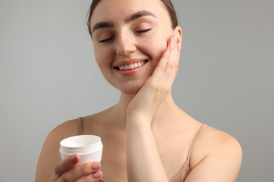 Photo of Beautiful woman with jar of face cream on gray background, closeup