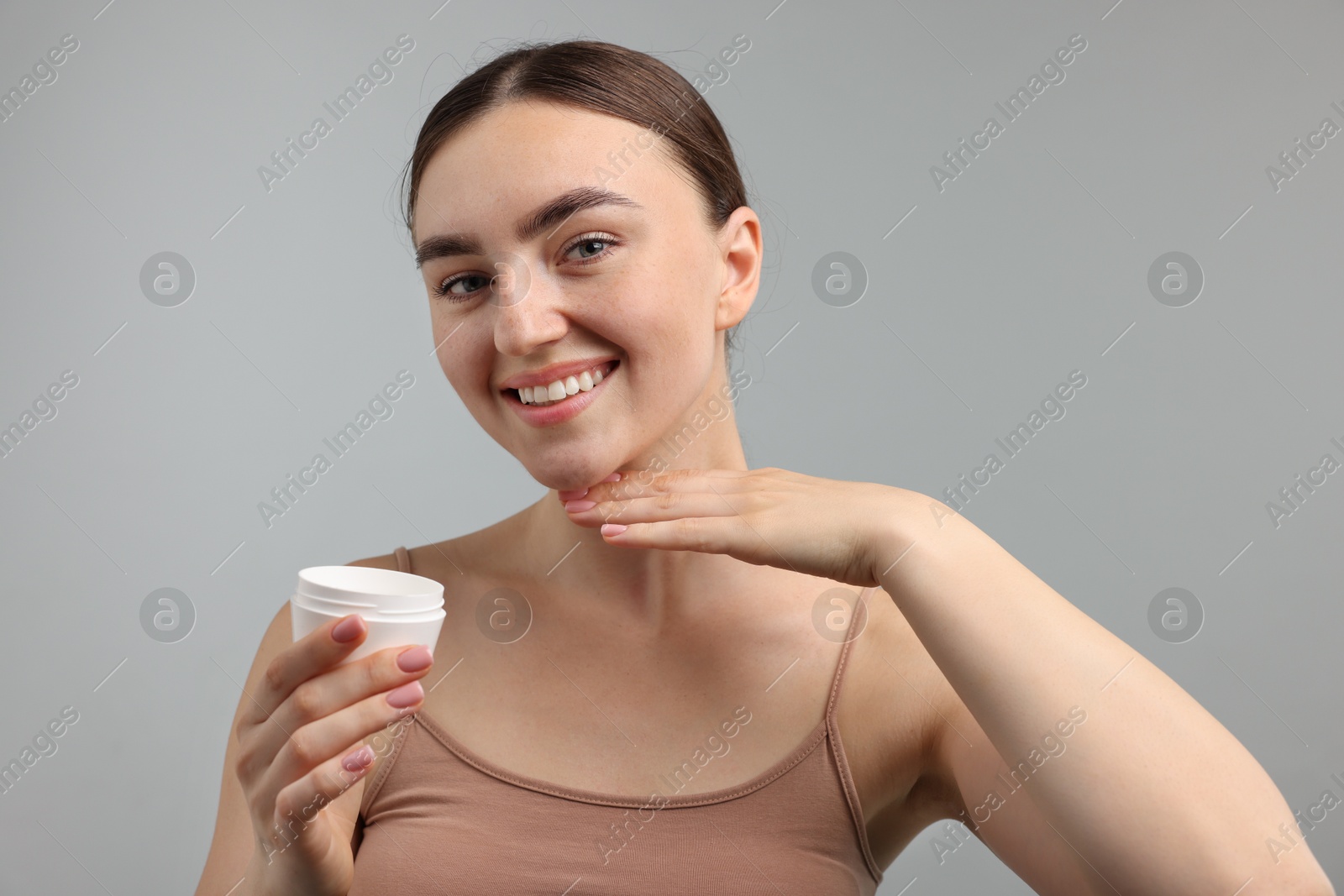 Photo of Beautiful woman with jar of face cream on gray background