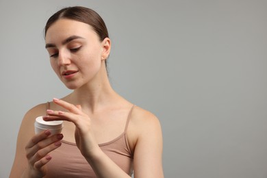Photo of Beautiful woman with jar of face cream on gray background. Space for text