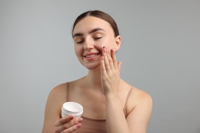 Photo of Beautiful woman applying cream onto her face on gray background