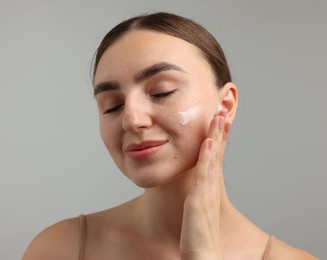 Photo of Beautiful woman applying cream onto her face on gray background, closeup