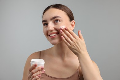 Photo of Beautiful woman applying cream onto her face on gray background