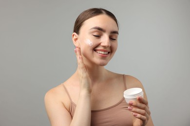 Photo of Beautiful woman applying cream onto her face on gray background
