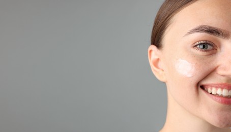 Photo of Beautiful woman with cream on her face against gray background, closeup. Space for text