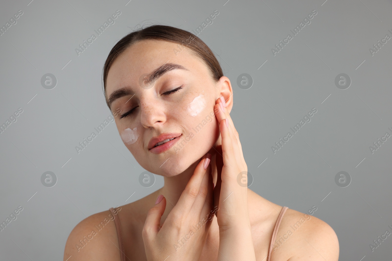Photo of Beautiful woman with cream on her face against gray background