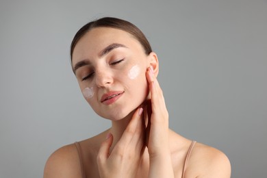 Photo of Beautiful woman with cream on her face against gray background