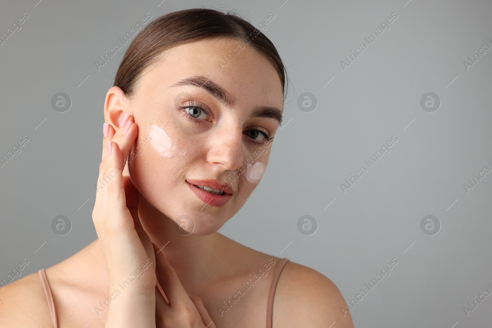 Photo of Beautiful woman with cream on her face against gray background, closeup. Space for text