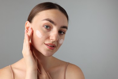 Photo of Beautiful woman with cream on her face against gray background, closeup. Space for text