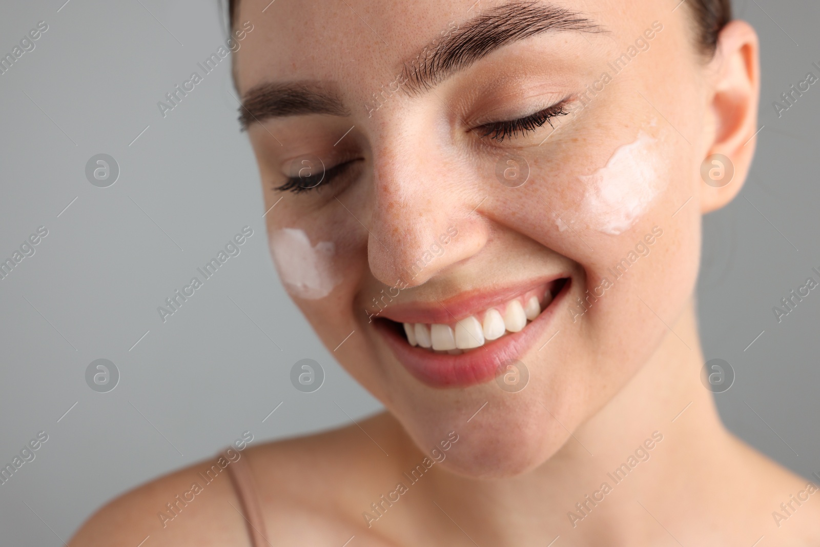 Photo of Beautiful woman with cream on her face against gray background, closeup