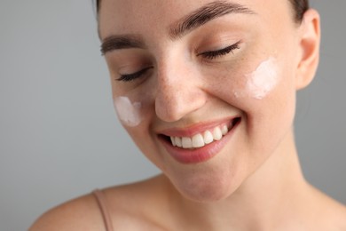 Photo of Beautiful woman with cream on her face against gray background, closeup
