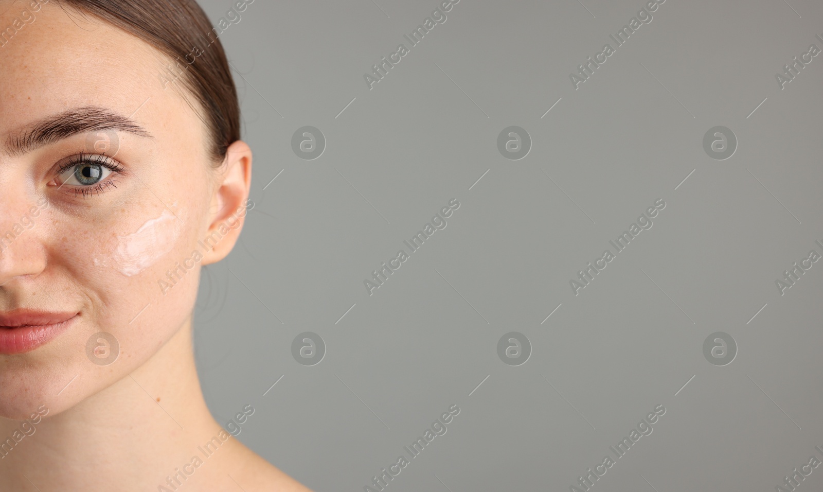 Photo of Beautiful woman with cream on her face against gray background, closeup. Space for text