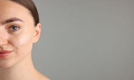 Photo of Beautiful woman with cream on her face against gray background, closeup. Space for text