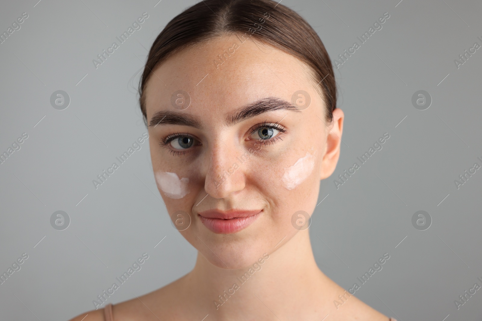 Photo of Beautiful woman with cream on her face against gray background, closeup