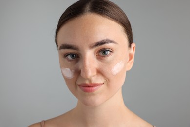 Photo of Beautiful woman with cream on her face against gray background, closeup