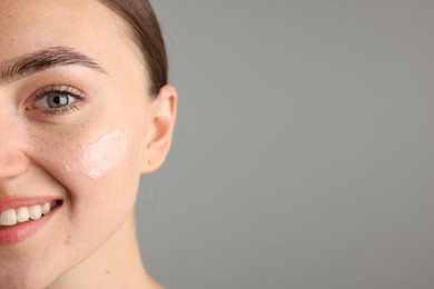 Photo of Beautiful woman with cream on her face against gray background, closeup. Space for text