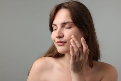 Photo of Beautiful woman applying cream onto her face on gray background