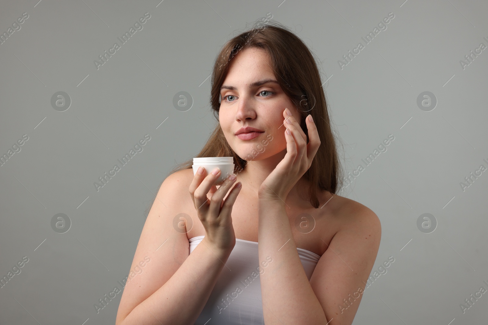 Beautiful woman applying cream onto her face on gray background Photo of Beautiful woman applying cream onto her face on gray background