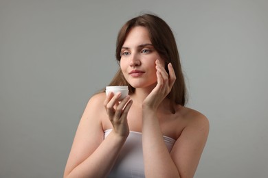 Photo of Beautiful woman applying cream onto her face on gray background