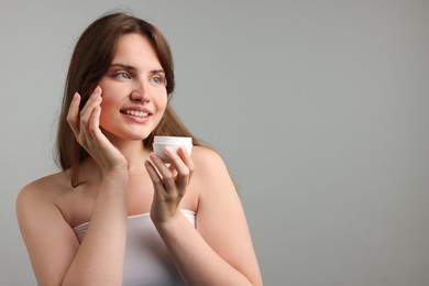Photo of Beautiful woman with jar of face cream on gray background. Space for text