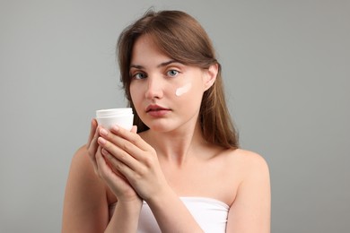 Photo of Beautiful woman applying cream onto her face on gray background
