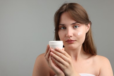 Photo of Beautiful woman applying cream onto her face on gray background. Space for text