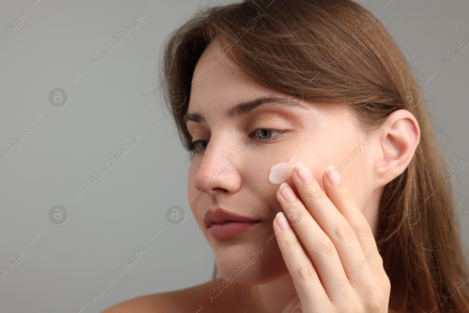 Beautiful woman applying cream onto her face on gray background, closeup. Space for text Photo of Beautiful woman applying cream onto her face on gray background, closeup. Space for text