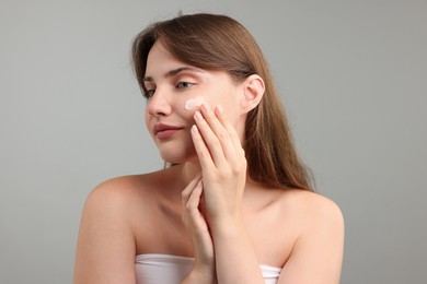 Photo of Beautiful woman applying cream onto her face on gray background
