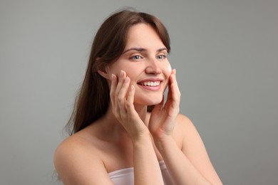 Photo of Beautiful woman applying cream onto her face on gray background