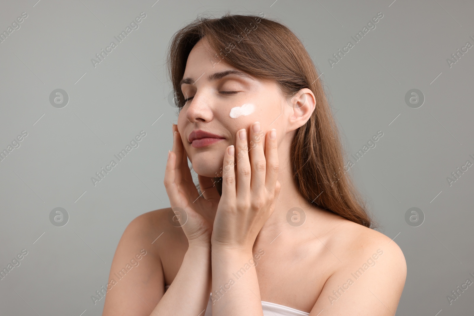 Beautiful woman with cream on her face against gray background Photo of Beautiful woman with cream on her face against gray background