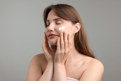 Photo of Beautiful woman with cream on her face against gray background