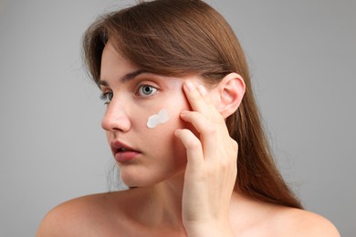 Photo of Beautiful woman with cream on her face against gray background, closeup