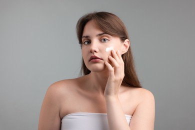 Photo of Beautiful woman applying cream onto her face on gray background