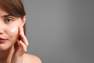 Photo of Beautiful woman with cream on her face against gray background, closeup. Space for text