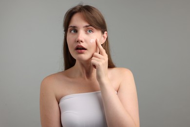 Photo of Beautiful woman applying cream onto her face on gray background