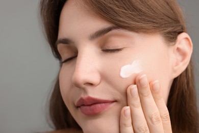 Photo of Beautiful woman with cream on her face against gray background, closeup