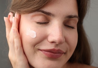 Photo of Beautiful woman with cream on her face against gray background, closeup