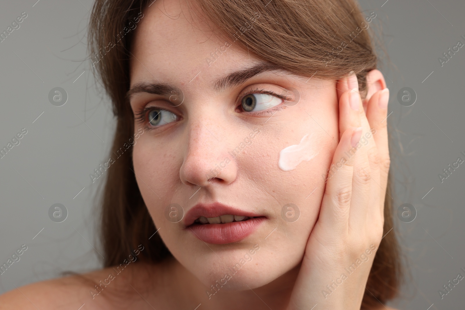 Photo of Beautiful woman with cream on her face against gray background, closeup