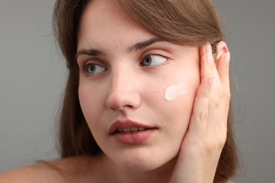 Photo of Beautiful woman with cream on her face against gray background, closeup