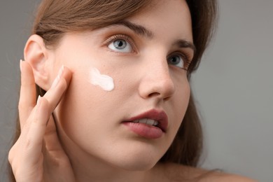 Photo of Beautiful woman with cream on her face against gray background, closeup