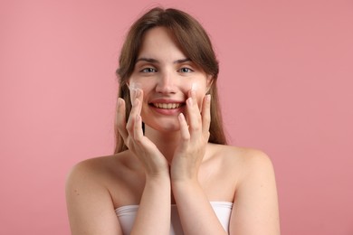 Photo of Beautiful woman applying cream onto her face on pink background