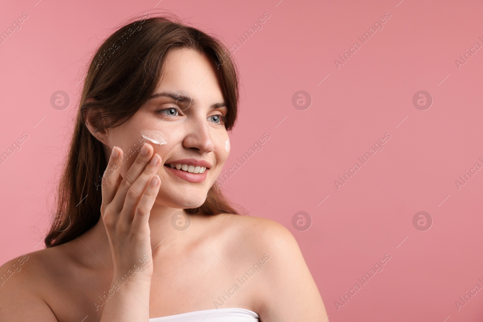 Beautiful woman applying cream onto her face on pink background. Space for text Photo of Beautiful woman applying cream onto her face on pink background. Space for text