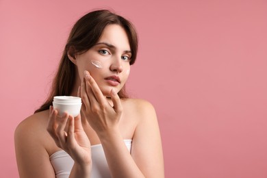 Photo of Beautiful woman applying cream onto her face on pink background. Space for text