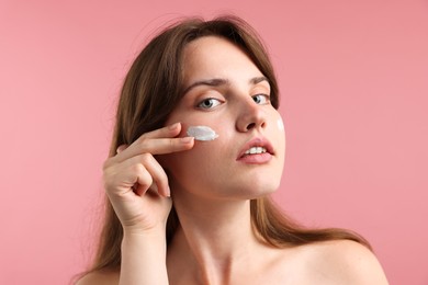 Photo of Beautiful woman with cream on her face against pink background, closeup