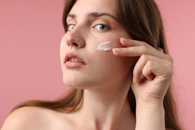 Photo of Beautiful woman with cream on her face against pink background, closeup