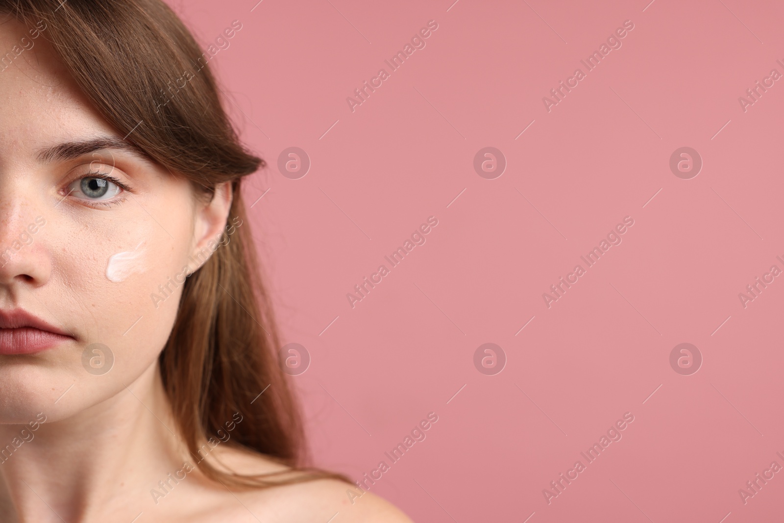 Photo of Beautiful woman with cream on her face against pink background, closeup. Space for text