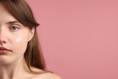 Photo of Beautiful woman with cream on her face against pink background, closeup. Space for text